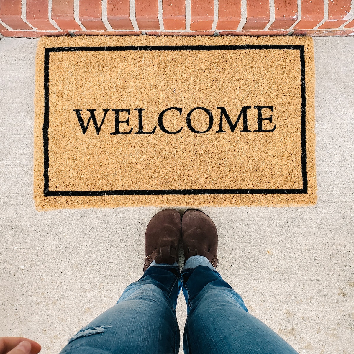 person in blue denim jeans standing on brown and black welcome area rug